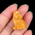 Carved yellow natural wolf crystal stone animal figurine held in hand on black background - Topaz