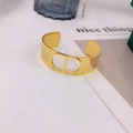 Bracciale rigido dorato lucido con iniziali intagliate su sfondo bianco minimalista - 31 Oro