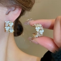Orecchini a fiore dorati con perle e zirconi indossati da una modella elegante - Fiore Bianco (Perla Artificiale Strass a C)