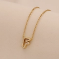 Macro shot of gold initial F pendant necklace with sparkling clear zircon pavé stones - Letter F