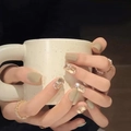 Gros plan de faux ongles courts verts et pailletés tenant une tasse à pois blancs - Brillance de Rêve (BY99)