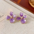 Detalle de pendientes de flores púrpuras con perla y bordes dorados sobre fondo de tela - Flor Púrpura (Aguja de Plata)