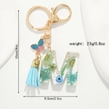Dettaglio portachiavi lettera M in resina con fiori secchi blu e ciondolo a farfalla - Lettera M