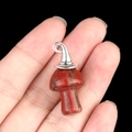 Red gemstone mushroom pendant with silver metal clasp held between fingers on black background - Silver Cap / Sesame Stone