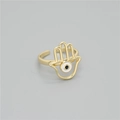 Detailansicht des goldenen Hamsa-Hand-Rings mit Emaille-Auge auf einem grauen Hintergrund - Hamsa mit weißem Auge