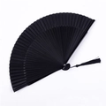 Gros plan d'un élégant éventail pliable en soie noire avec un pompon décoratif assorti - Éventail en Bambou Premium Noir Solide Sans Creux