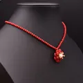 Rote Korallenperlenkette mit goldenem Blumenperlenanhänger auf einem schwarzen Display - Koralle Perlenhalskette