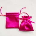 Detail of two glossy rose red satin drawstring gift bags on a white textured surface - 12x14cm / Rose Red