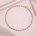 Detail of gold chain necklace with pink evil eye beads on soft pink fabric background - Purple