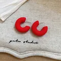 Macro view of matte red C-shape stud earrings with silver pins on a beige linen background - Red Round