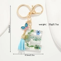 Detail of resin letter E keychain with dried flowers, evil eye, and blue tassel charms - Letter E