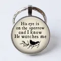 Silver round glass keychain featuring His Eye is on the Sparrow inspirational text - Sparrow Illustration/He watches me