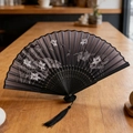 Classic black folding fan featuring white lotus pattern and decorative black silk tassel - Dragonfly Lotus