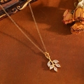 Gros plan du collier pendentif feuille serti de pierres marquises sur fond vintage - Collier feuille dorée (T029)