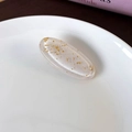 Gros plan d'une pince à cheveux ovale en résine avec feuilles d'or sur plat en porcelaine - crème