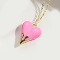 Makroaufnahme von rosa Emaille-Herzanhänger mit goldenen Tropfendetails an feiner Kette - Rosa
