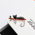 Charming enamel cat brooch with black and white spots resting on a red branch pin - Black Spotted Cat (269)