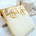 Close-up of golden bow earrings with vintage brushed metal texture on a beige stand - Brushed Texture Style / Gold-Wide Bow