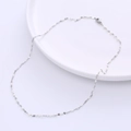Detail of silver titanium chain necklace with white enamel beads on a white ceramic plate - Steel + White Enamel