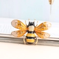 Elegant gold-tone bee brooch with yellow enamel wings and crystal accents on book page - Bee / Yellow