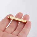 Macro detail of a golden stainless steel rectangular bar pendant held by fingers for scale - 18K Gold