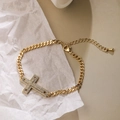 Dettaglio del bracciale a croce placcato oro con zirconi su sfondo materico - Stile Croce Svuotata con Pavé di Strass (31592)