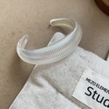 Macro detail of a translucent ribbed open bangle on a beige linen studio background - Iridescent - Fine Texture