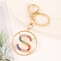 Close-up of golden letter S keychain with colorful rhinestones on white plate - S
