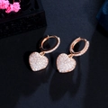 Macro shot of rose gold heart earrings with zircon inlay on a dark textured surface - White