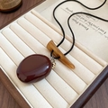 Detailed shot of vintage necklace with deep red stone pendant and small golden acorn charm - Reddish Brown Pebble Style