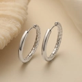 Elegante silberne Creolen mit Innenstruktur auf minimalistischem beigem Hintergrund - Silber