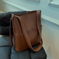Braune Leder-Eimertasche mit Kontrastnähten und verstellbarem Riemen auf dem Sofa - Hellkaffee
