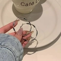 Detail showing hand holding silver twisted hoop earrings against a cafe table background - S925 Silver Needle Earrings - Silver Twisted Design
