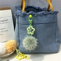 Close-up of a blue and green plush star charm on a denim handbag with yellow handles - Green