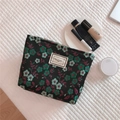 Flat lay of floral canvas makeup bag with cosmetics on a white quilted background - Black
