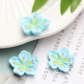 Three blue resin cherry blossom DIY accessories with yellow stamens on a white plate - Blue