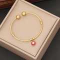 Gold open bangle with red evil eye enamel charm displayed in a beige jewelry gift box - Red
