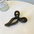 Draufsicht auf eine glänzend schwarze Haarklammer mit Schleife auf weißem Tisch - Dunkelgrau