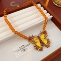 Detailansicht einer orangefarbenen Perlenkette mit einem Emaille-Schmetterlingsanhänger - Schmetterling Perlenhalskette / Gold-Gelb