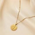 Detailed close-up of a gold embossed coin pendant on a beaded chain over silk fabric - Virgo