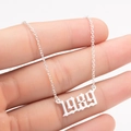 Close-up of gothic silver 1989 birth year necklace pendant on a cross chain held by hand - 1989 / Steel