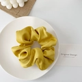 Detail of a ginger yellow satin scrunchie displayed on a ceramic plate with decor - Gold