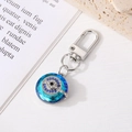 Detailed view of evil eye keychain with blue crystal on a textured stone surface - Silver Round Eye