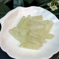 Close-up of translucent light green crystal stone strips in a white shell-shaped dish - Citrine