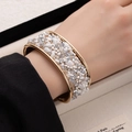 Close-up of wide gold cuff bracelet featuring white crushed stones and sparkling crystals - White