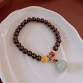 Detail eines Granatperlenarmbands mit grünem Jade-Lotus-Anhänger auf einem Keramikteller - Hetian Jade Granat Bienenwachs Perlenarmband