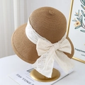 Elegant wide brim straw hat with white lace bow decoration on a gold display stand - One Size / Khaki