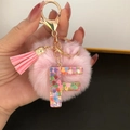 Close-up of pink pompom keychain with resin letter F filled with heart sequins - Letter F