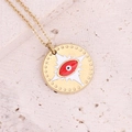 Close-up of golden necklace featuring a red eye charm with star motifs on stone surface - Red