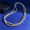 Primer plano de un elegante collar largo de perlas con brillo intenso sobre fondo azul - Gris